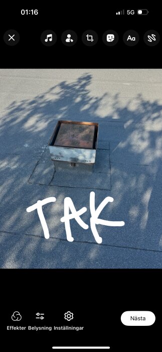 Ventilationshål med metallkåpa på papptak, markerad med texten "TAK". Skuggor från träd syns på taket.