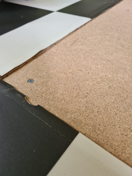 Spånskiva bredvid schackrutigt plastgolv i kök, visar nivåskillnad efter att skåp tagits bort och golvet justerats för diskmaskinsinstallation.