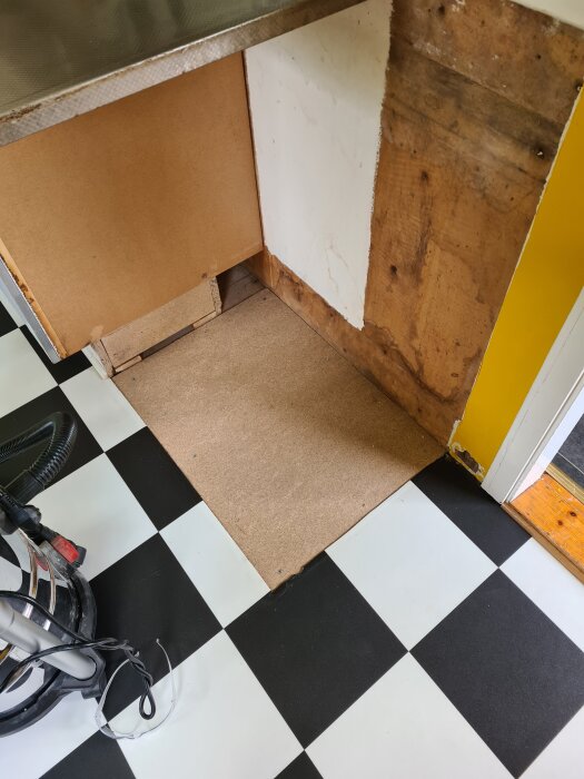 Tomt utrymme under diskbänk med spånskiva lagd över undergolv i randigt kök, redo för installation av diskmaskin.