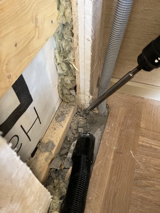 Vägghörn med borr, isolering och byggmaterial under montering av skåp.