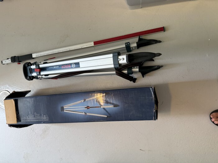 Tripod och mätpinne från Bosch, i nyskick. Dessa används för att bygga en mur och ligger bredvid en öppnad kartong. Finns i Jönköpingsområdet.