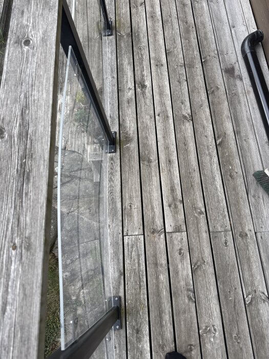 Balkongräcke i genomskinlig plast med trätrall på golvet, fastskruvat i metallstöd, vy från ovan.