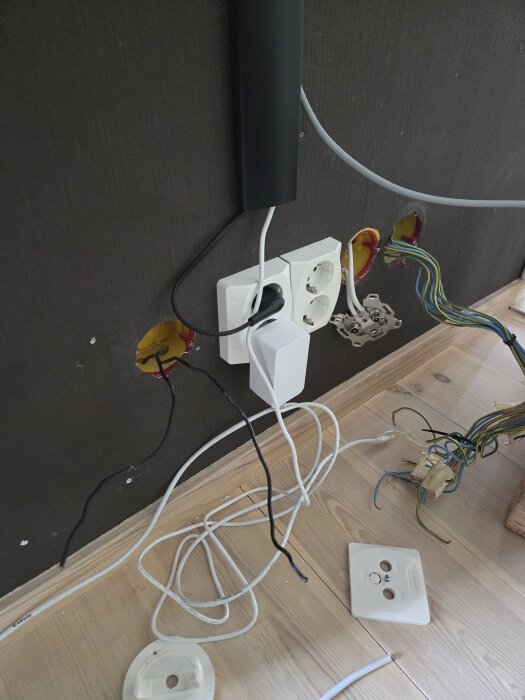 Vägg med eluttag, exponerade kablar och öppna apparatdosor; två svarta kablar sticker ut från väggen.