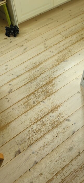 Vitbetsat furugolv med synligt slitage och repor efter åtta års användning i kök och matplats.