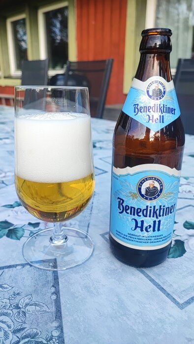 Flaska och glas med Benediktiner Hell öl på ett bord utomhus.