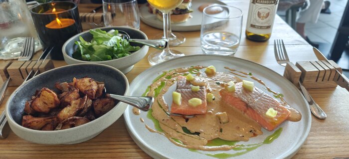 Tallrik med röding, rostad potatis och sallad på ett bord, serverad med dryck.