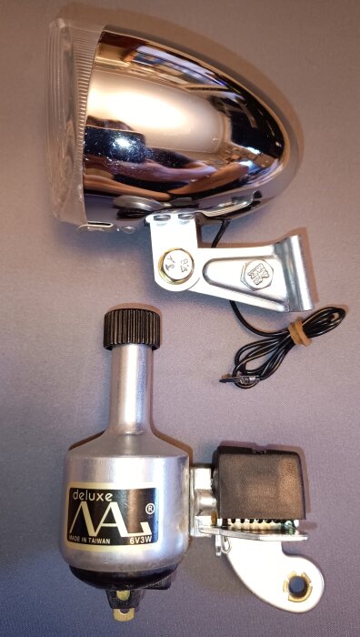 Cykelbelysning med dynamo av märket Deluxe, inklusive lampa och generator, placerad på ett bord.