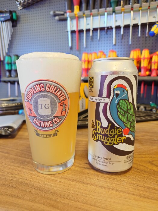 En ölburk "The Budgie Smuggler" och ett glas med skummande IPA, verktyg synliga i bakgrunden.