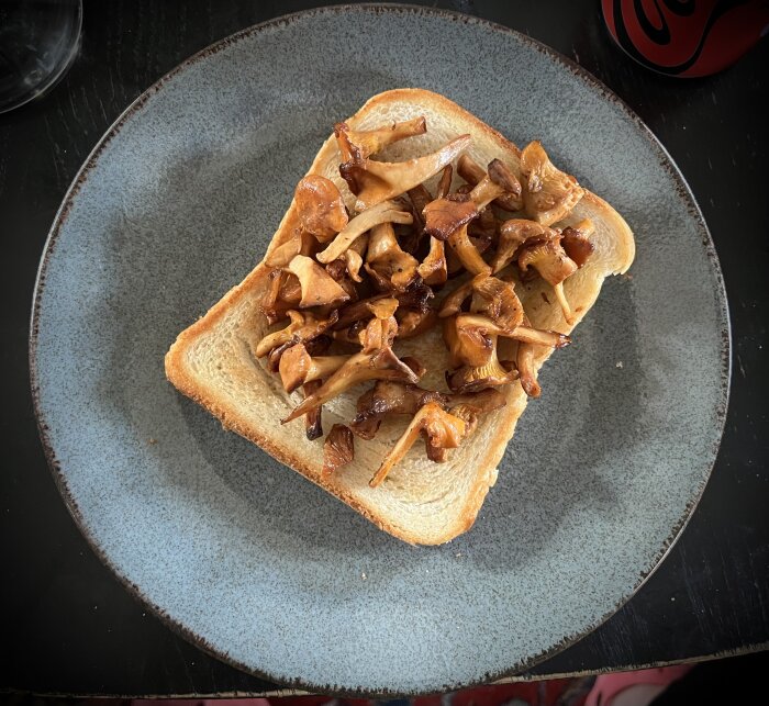 Skiva rostat bröd toppat med kantareller på en tallrik.
