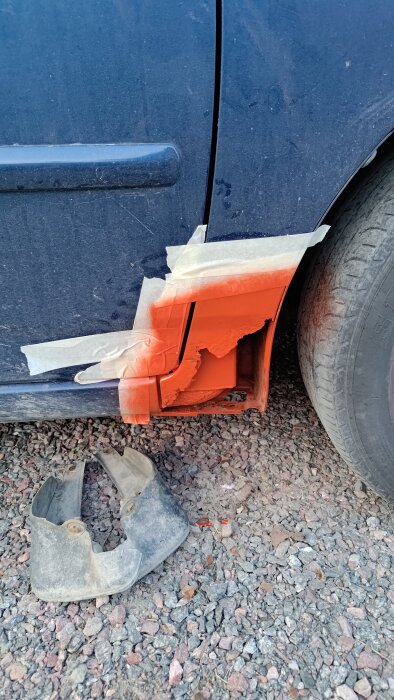 Bilens hjulhus med målartejp och orange färg, intill ligger en avmonterad stänkskärm.