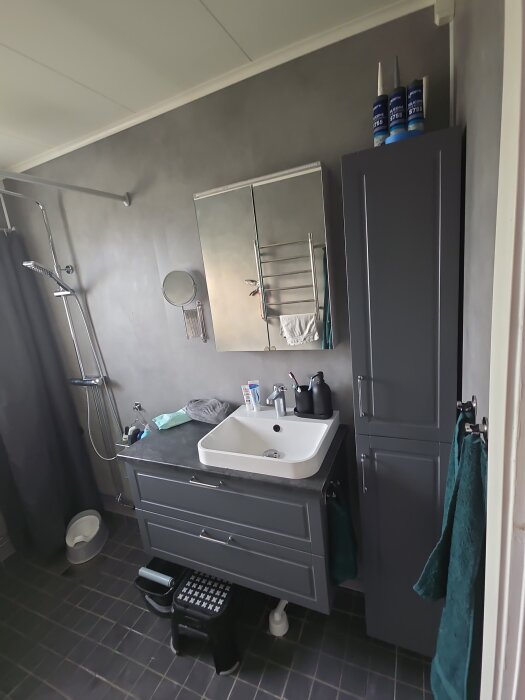 Modernt badrum med grå skåp, spegel, dusch och handfat. En del av ett nyrenoverat projekt. Golvet är ännu ej polerat.