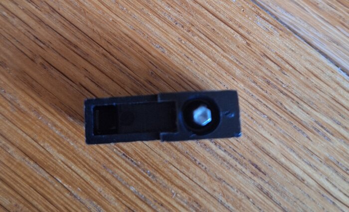 Svart plastvred med metallaxel formad som en hexnyckel på ett träbord, relaterat till Ballofix-ventil.