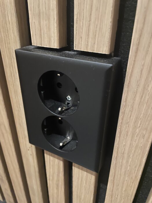Eluttag i svart ram monterat i nivå med panel, utan förhöjningsring.