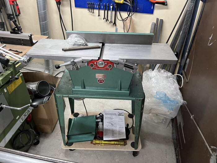 En Hammerhyvel står i ett garage, med verktyg och instruktioner på bordet. Bakgrunden visar fler verktyg och förvaringslådor.