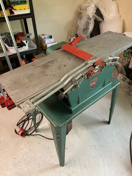 Grön och röd Hammerhyvel maskin i ett garage med hyllor i bakgrunden, redo att ges bort efter renovering.