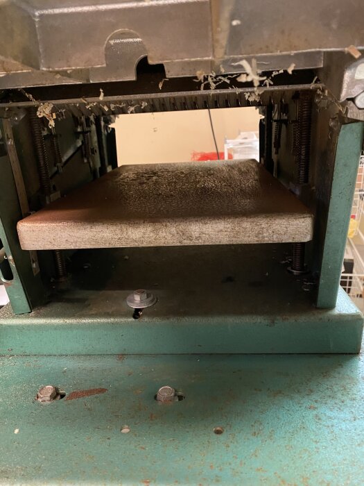 Närbild av insidan på en hammerhyvel, visar hyvlingsmekanismen och träspån. Maskinen ser använd och lite dammig ut.