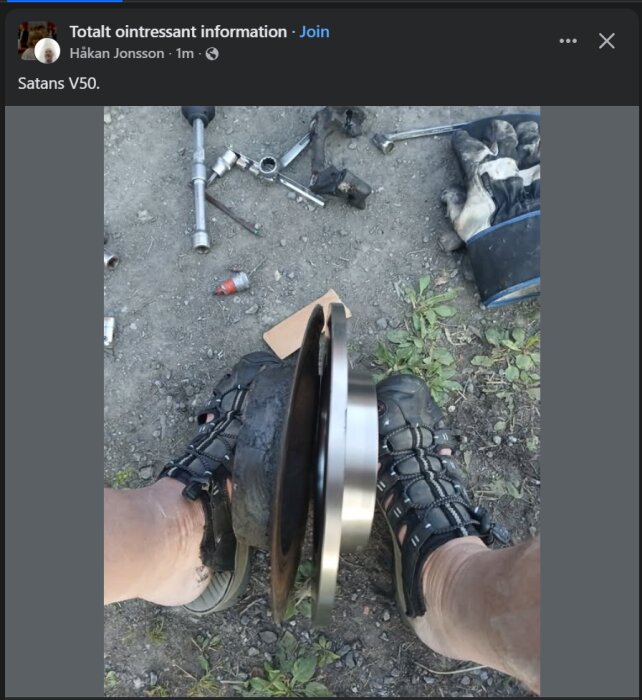 Bild av slitna och nya bromsskivor på marken, mellan en persons sandalklädda fötter. Olika verktyg och handskar syns i bakgrunden.