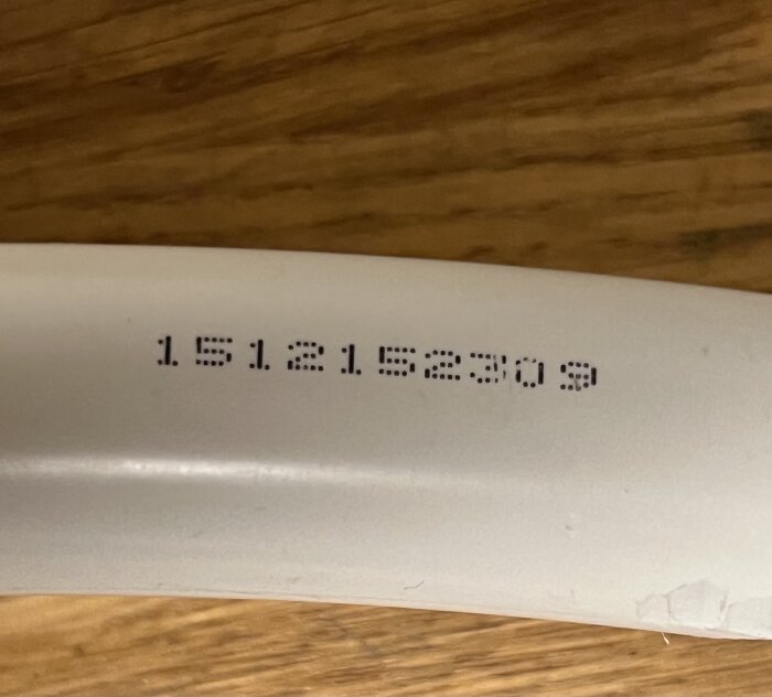 Nummer kod tryckt på ett vitt rör, synlig text: 1512152303, delvis avskavd.