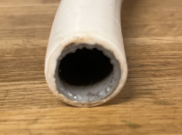 Närbild av ett vitt rör med avskavd yta, visandes dess öppna ände och innandöme. Röret ligger på en träyta.