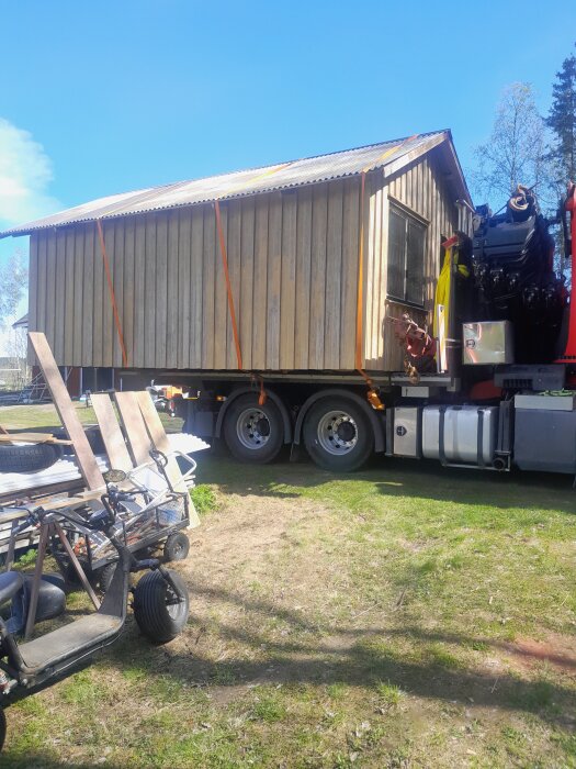 En trälada fastspänd på en lastbil, nyanländ på en gräsmatta under en klarblå himmel.