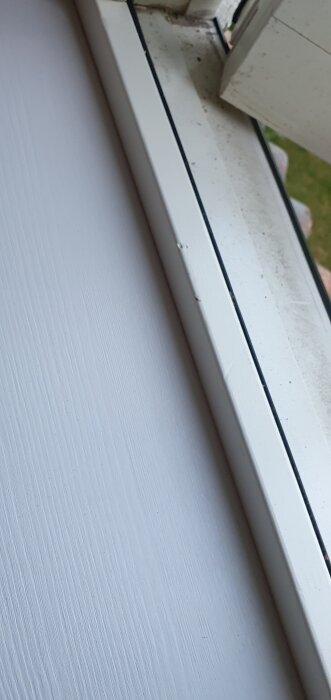 Närbild av ett fönsterkarm och vägg med en liten springa mellan karm och väggbräda.