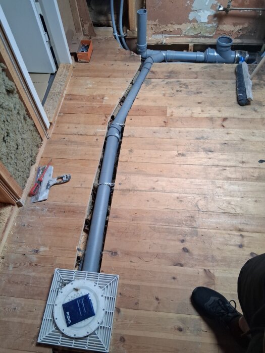 Golvbjälklag med uppkapade golvelement och synliga rör för golvbrunnen på övervåningen, verktyg och instruktioner syns också.