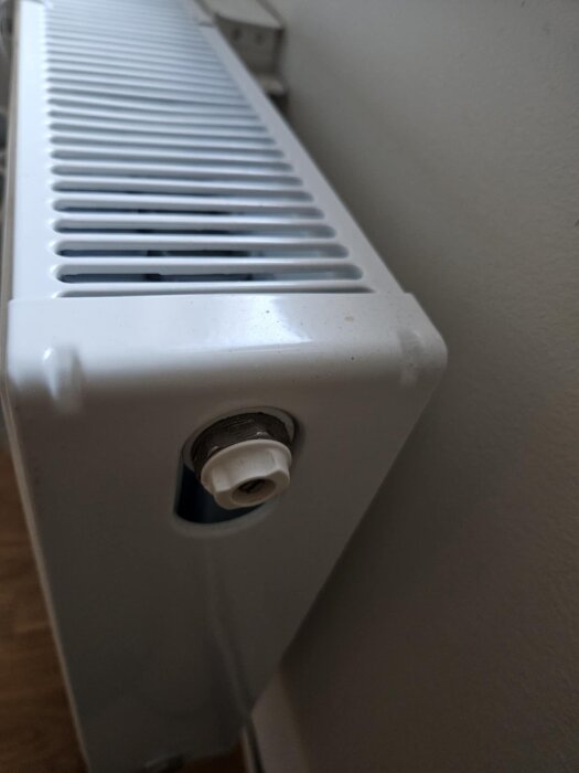 Vitt element sett från sidan, med fokus på termostatventil mot en ljus vägg.