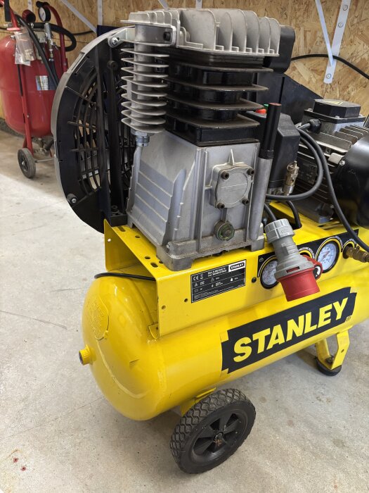 Gul Stanley luftkompressor i ett garage, med frågor om anslutningstyp och gängstorlekar på kopplingarna.