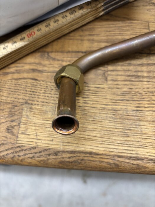 Kopparrör med mässingskoppling fotograferat på ett träbord, bredvid en linjal.