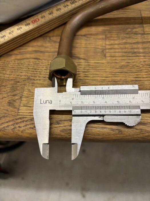 Mätning av kopparrörs anslutning med skjutmått på träbord.