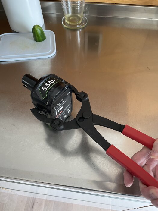 Verktyg med rött handtag används för att ta loss ett stort Ryobi 5.5Ah batteri på en köksbänk.