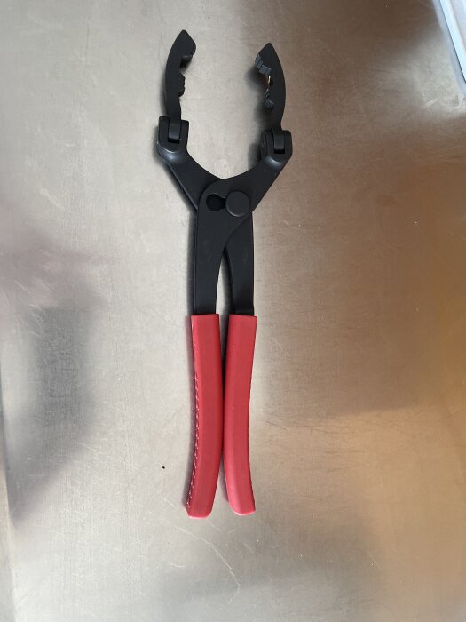 Tång med röda handtag, använd för att lossa stora Ryobi-batterier, liggandes på en metallisk yta.