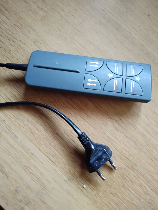 Fjärrkontroll och elkontakt till höj- och sänkbar säng på träbord.