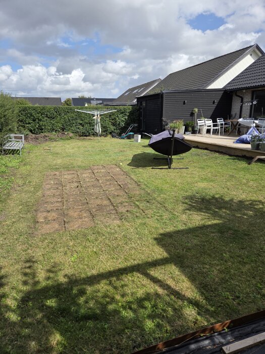 Nyplanerad gräsmatta framför ett hus, med möbler på altan och en torkvinda, efter att ogräset har avlägsnats och jorden bearbetats.