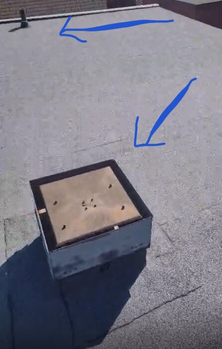 Takkonstruktion med fyrkantig enhet i förgrunden och rörformad del längre bort, markerade med blå pilar.