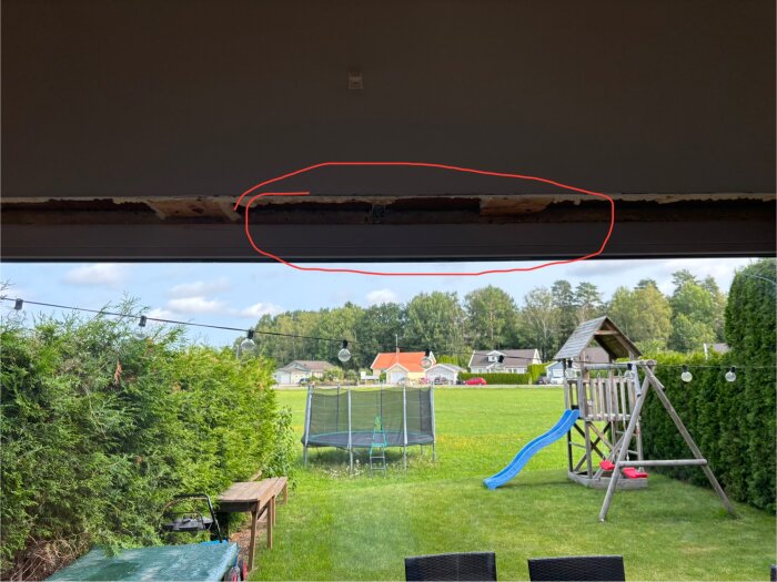 Bild av fuktskadad isolering runt fönster i ett radhus. Skadan inringad med rött, utomhusmiljö med trädgård och lekplats i bakgrunden.