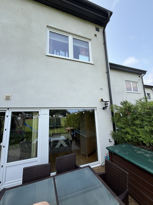 Tvåvånings radhus med vit fasad, stora fönster och trädgårdsmöbler på uteplats.