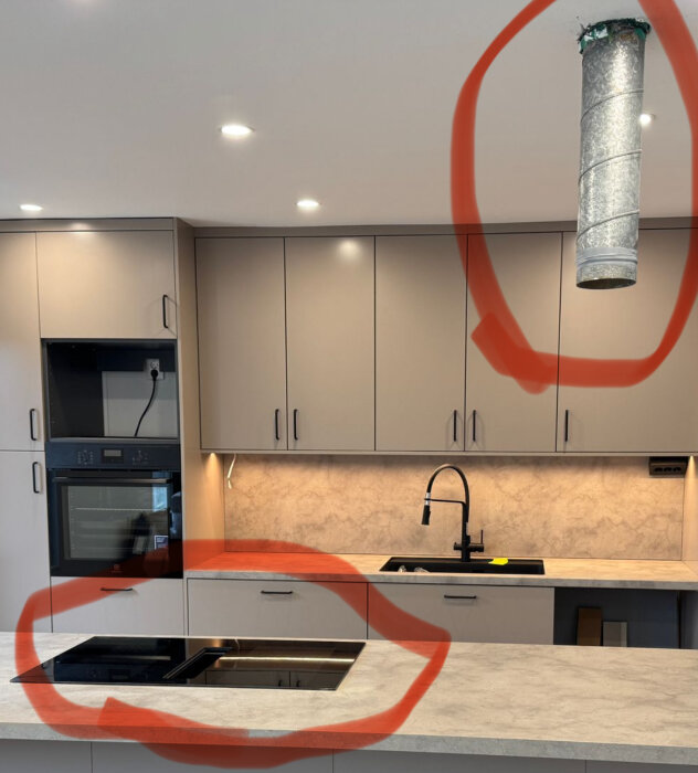 Kök med cirklat ventilationsrör i taket och cirklat område på bänkskivan där en häll är installerad, omgiven av ljusa skåp och diskho.