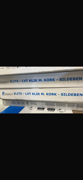 Förpackningar med texten "Elite - LVT Klik m. Kork - Sildeben" från Migadan A/S, troligen vinylgolv med klicksystem.