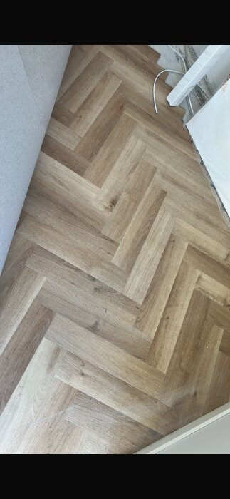 Vinylgolv i fiskbensmönster med ljusa och mörka trätoner, oinstallerat i ett rum under renovering.