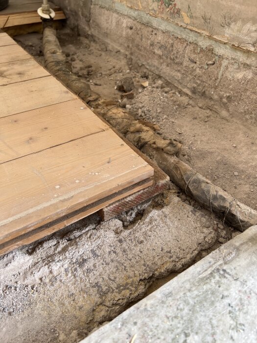 Betonggolv under gammalt trägolv som delvis har tagits bort, visar rör och betongbjälklag från 1939.