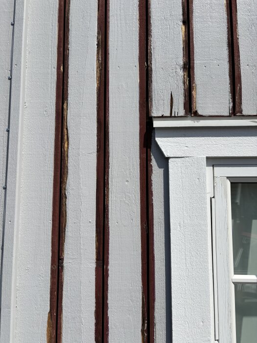 Sliten fasad med hårt angripna lockläkt på en gavel, där träet är mjukt och delvis bortskrapat. Fönster till höger.