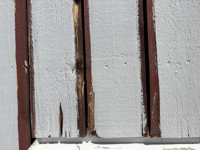 Skadade bottenbrädor på fasad, med spruckna och mjuka kanter, där lockläkten avlägsnats för att undersöka skador och möjlig reparation.