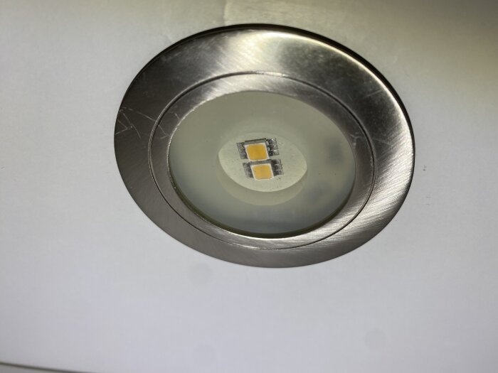 Inbyggd downlight-lampa i rostfri ram, fotograferad från nära håll, visar fyra LED-dioder under ett frostat glas.