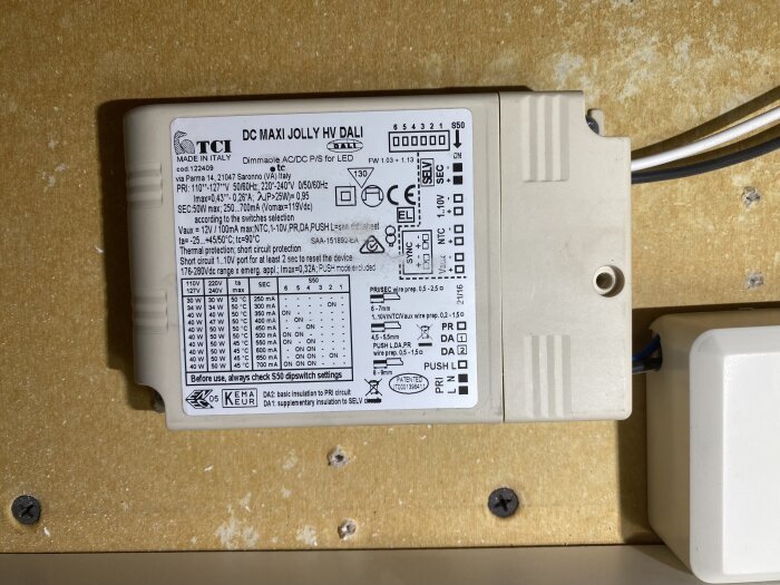 Bild på en vit DC Maxi Jolly HV DALI driver med text och tekniska specifikationer synliga på ovansidan, monterad på träyta.