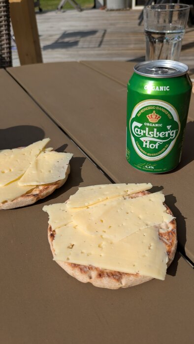 Smörgåsar med ost bredvid en burk Carlsberg Hof öl på ett bord utomhus.