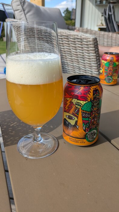 Ett glas med grumlig öl och en färgglatt designad burk märkt "Amundsen Apocalyptic Thunder Juice", placerade på ett utebord.