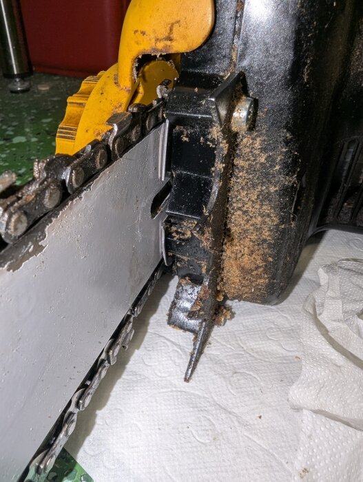 Bild på en motorsåg med synlig kedja och svärd, där en möjlig skruvplats markeras med smuts på kroppen av sågen.