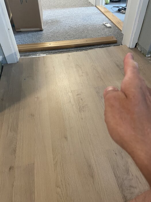 Hand pekar på nylagt klickgolv som rest sig vid dörrposten. Tecken på fel i installationen, saknar rörelsemån. Diskuteras eventuell åtgärd.