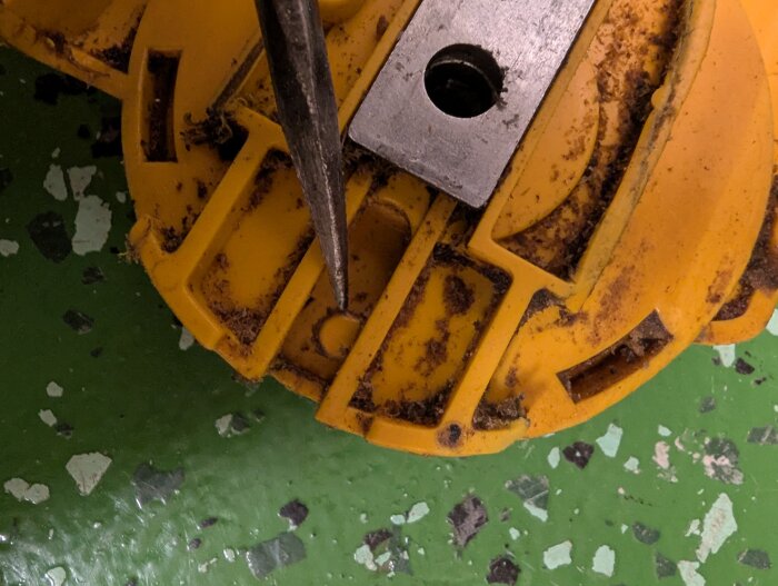 Gult plastvred med spiralformad kant, fastsatt på grön yta med metallstav igenom, visar mekanismen som minskar spåret vid rotation.